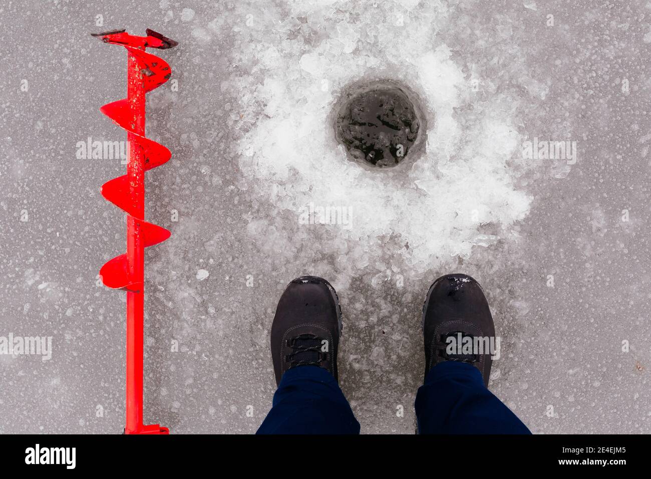 Vue du trou de glace, des bottes d'homme et de la vis à glace rouge. Pêche d'hiver sur le lac. Concept de pêche sous la glace Banque D'Images