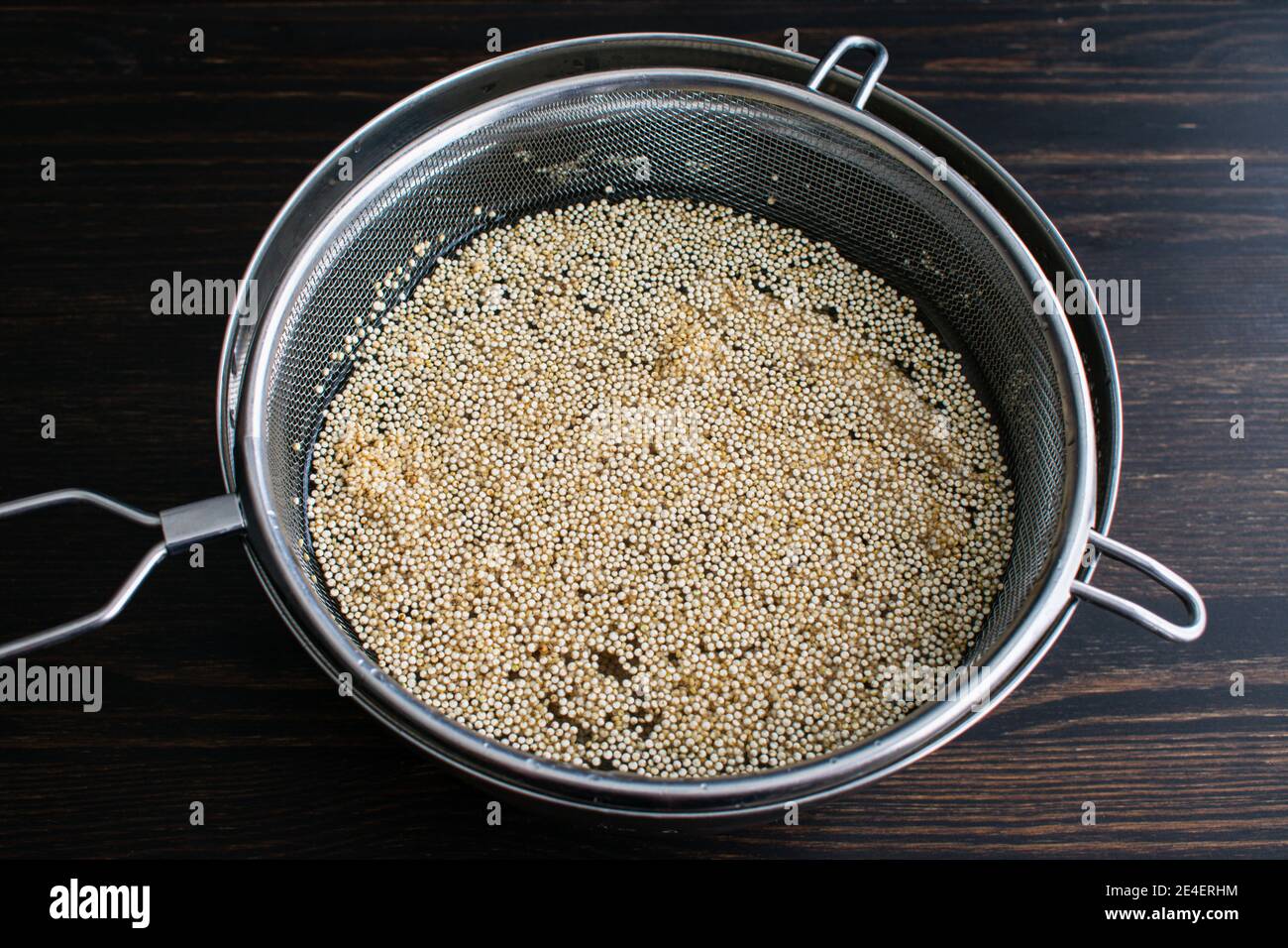 Rinçage du quinoa blanc dans l'eau : rinçage des grains de quinoa non cuits dans une crépine placée sur un bol de mélange Banque D'Images