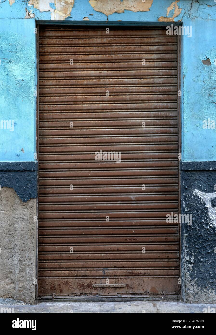 détail d'une porte fermée avec un vieux et rouillé obturateur sur une ancienne façade avec un bleu et détérioré mur Banque D'Images