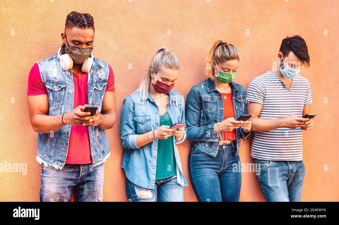 Amis multiraciaux avec masques de visage fermés à l'aide de l'application de suivi avec Smartphones mobiles - jeunes gens du milieu partageant du contenu sur les réseaux sociaux réseau multimédia Banque D'Images