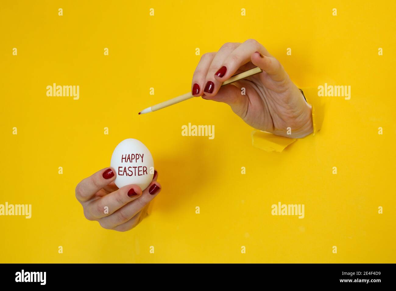 Joyeux thème abstrait Pâques. Les mains peignant un oeuf blanc de pâques tout en brisant à travers les découpes d'un fond de carton jaune Banque D'Images