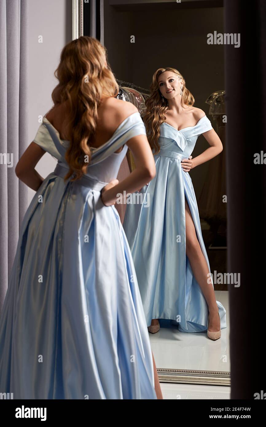Jeune belle fille blonde portant une robe de bal de bal de bal de bal de bal  de proéminent bleu satiné hors de l'épaule. Modèle en miroir. Cabine  d'essayage dans la robe