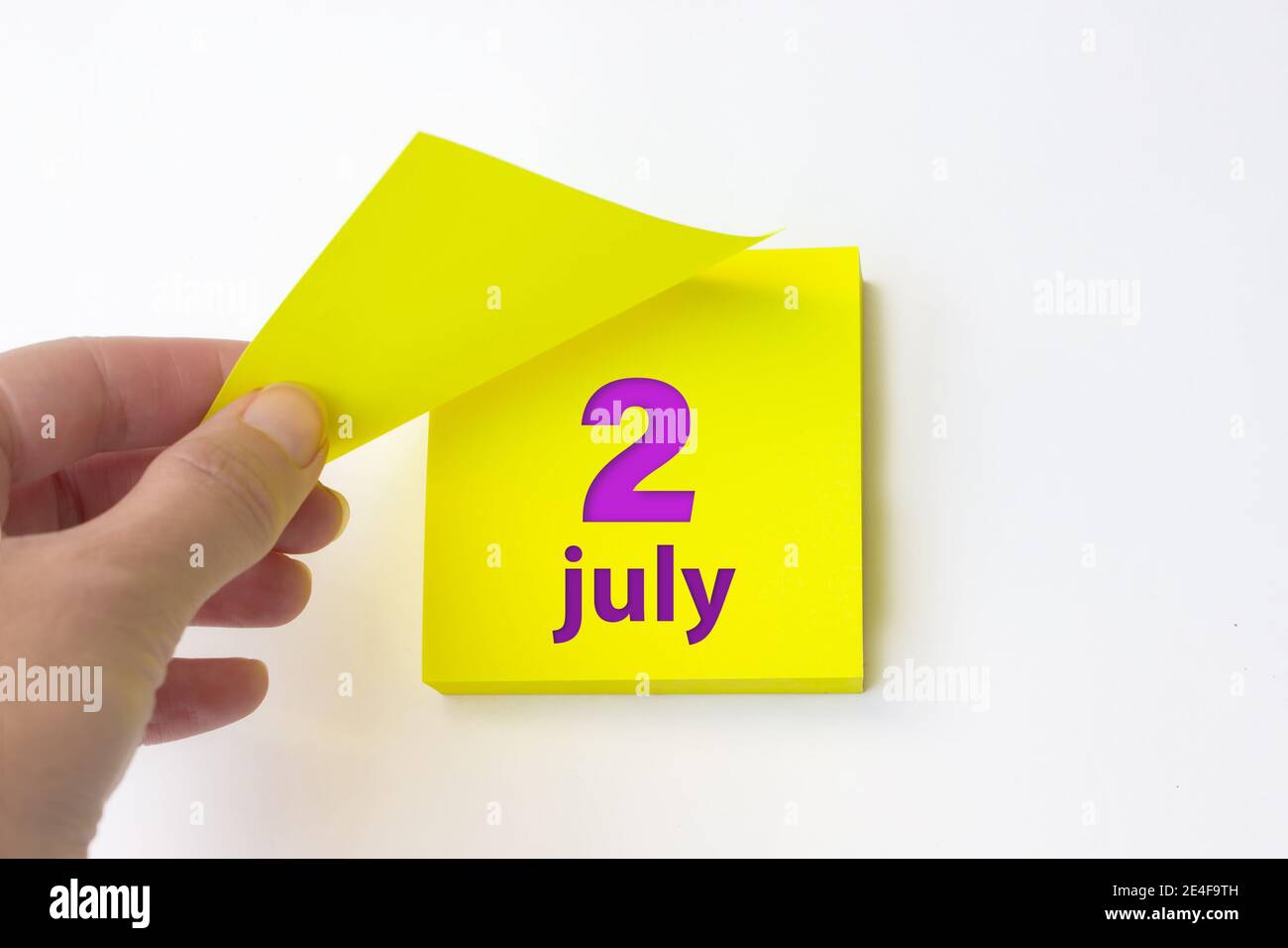 2 juillet. Jour 2 du mois, date du calendrier. La main se défait de la feuille jaune du calendrier. Concept mois d'été, jour de l'année Banque D'Images