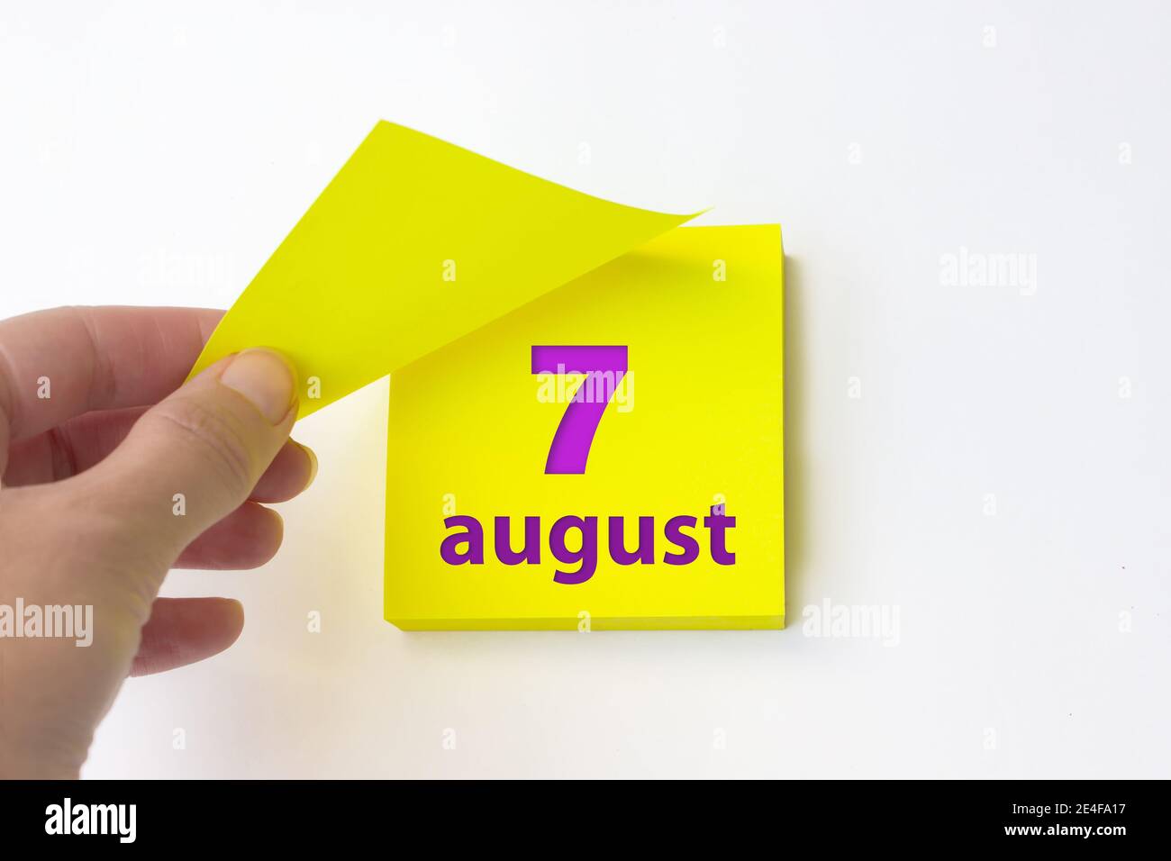 7 août. Jour 7 du mois, date du calendrier. La main se défait de la feuille jaune du calendrier. Concept mois d'été, jour de l'année Banque D'Images