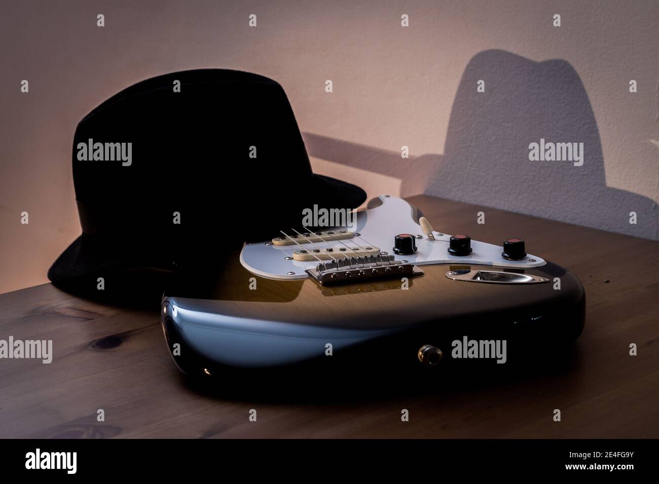 Une guitare électrique et un chapeau noir sur une table un soir. Banque D'Images