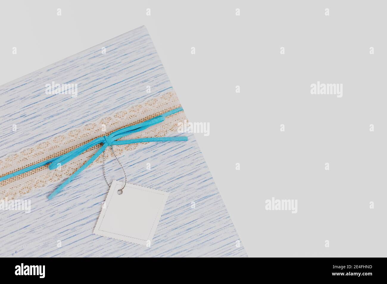 Fragment de boîte cadeau avec noeud en daim bleu et carte en papier blanc vierge sur fond isolé, touche basse toile de fond, couleurs pastel Banque D'Images
