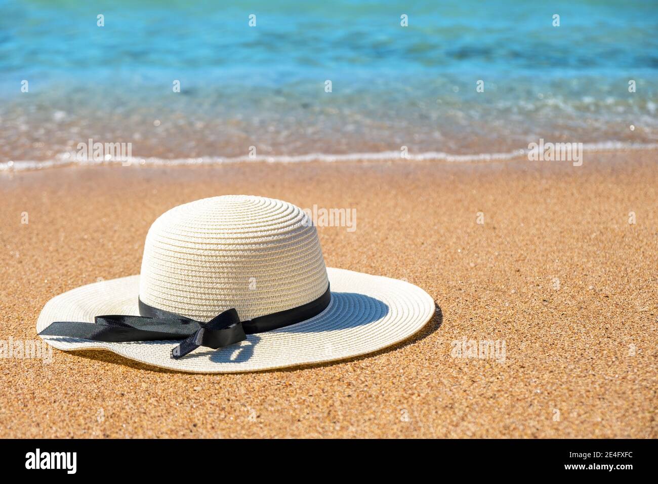 Chapeau de paille femme blanc posé sur la plage de sable tropical avec de  l'eau bleue vive en arrière-plan le jour ensoleillé de l'été. Vacances et  voyage de destination Photo Stock -