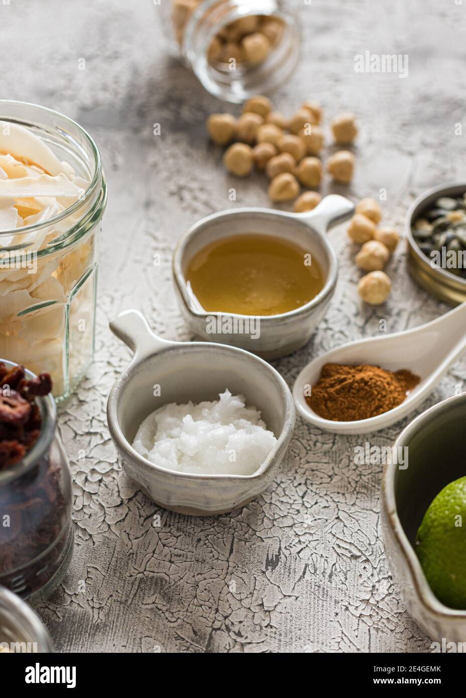 Quelques ingrédients crus de granola dans des bols et des pots en verre avec de l'huile de cacao et du miel au milieu. Banque D'Images