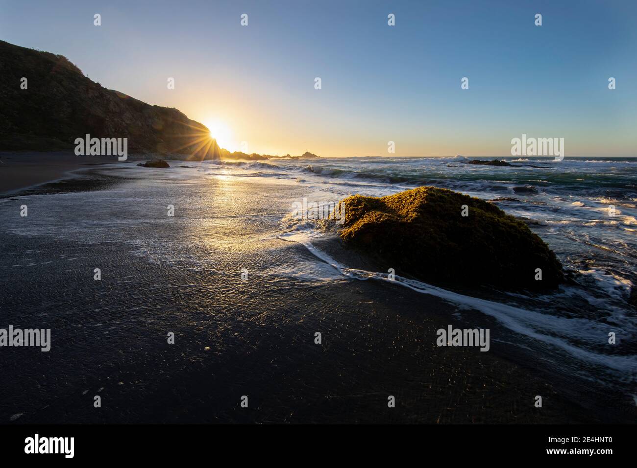 Un incroyable coucher de soleil sur l'eau avec les vagues qui éclabousse l'eau vers les rochers et les algues. Un paysage idyllique et coloré dans une plage sauvage Banque D'Images