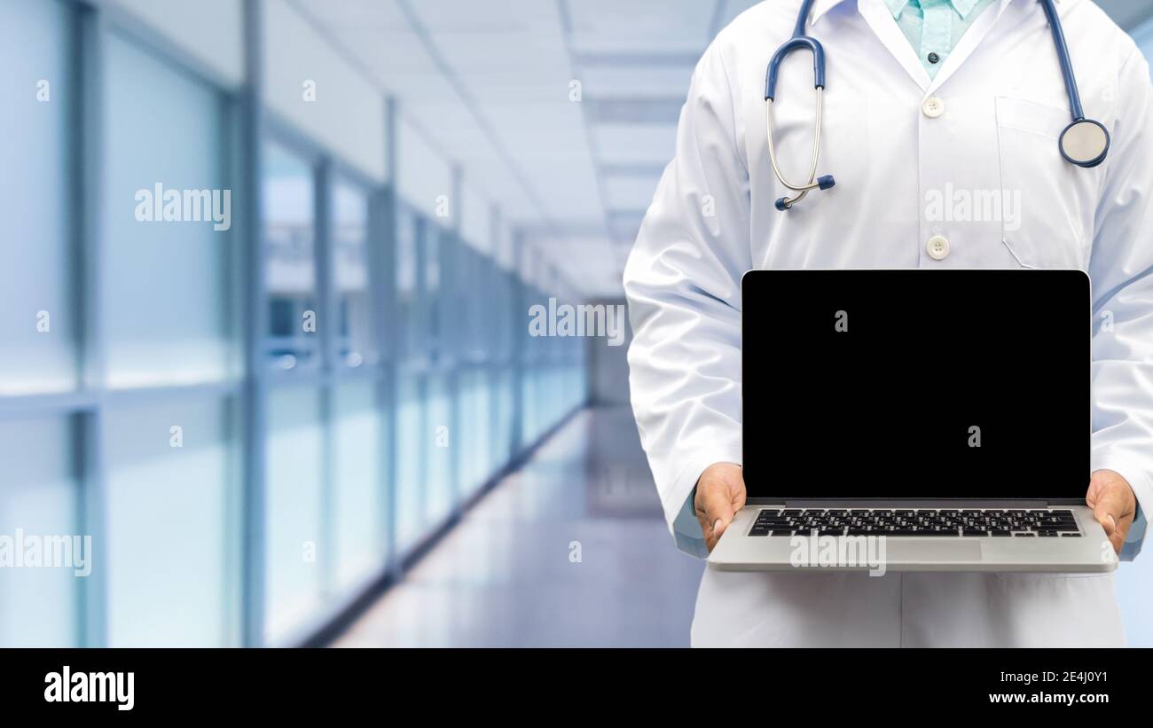 Médecin tenant l'ordinateur portable en vue avant droite avec un arrière-plan flou de l'hôpital. Mise au point sélective sur l'écran de l'ordinateur. Médical et santé Banque D'Images