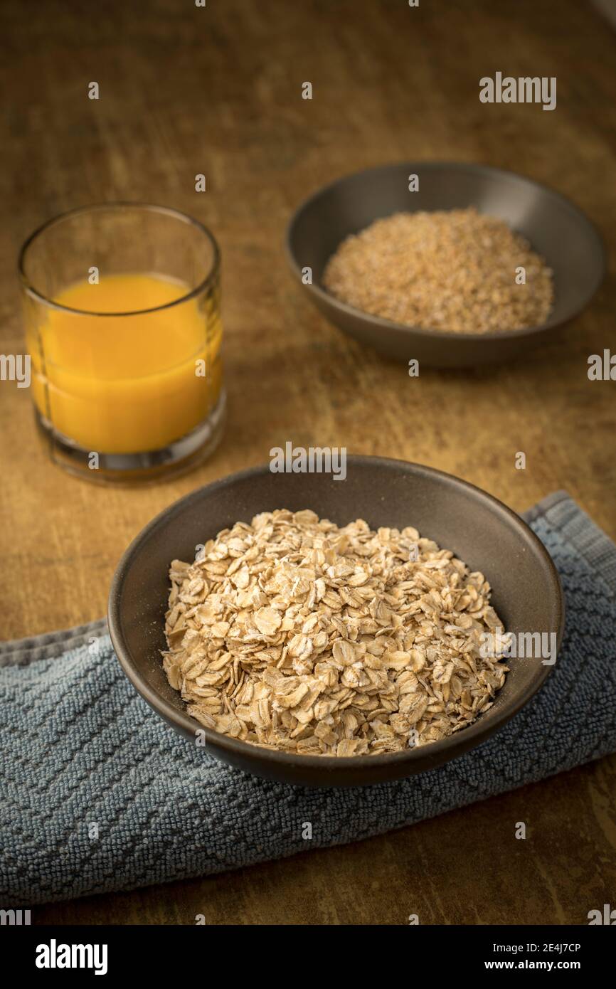 Un gros plan de flocons d'avoine séchés et de l'avoine coupée en acier dans des bols avec un verre de jus d'orange. Banque D'Images