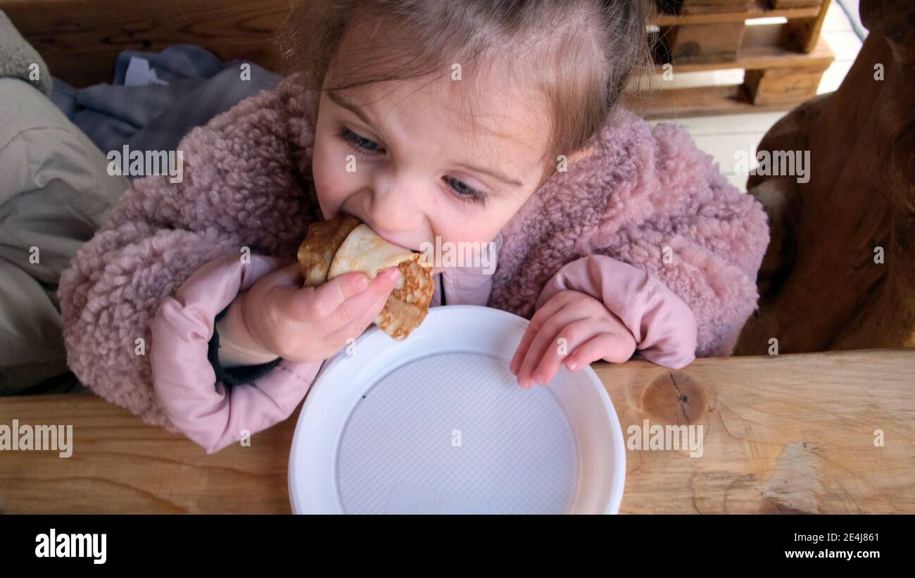 Adorable petite fille mange de délicieuses crêpes fraîches dans un cadre rustique table en bois dans un café confortable Banque D'Images