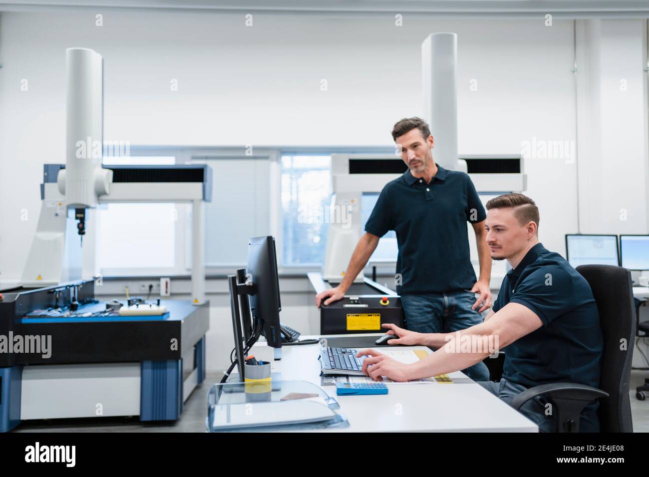 Un technicien de sexe masculin avec un collègue utilisant un ordinateur dans un bureau industriel Banque D'Images