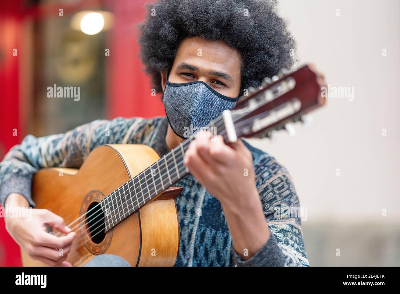 Jeune homme portant un masque de visage jouant de la guitare tout en étant assis à l'extérieur Banque D'Images