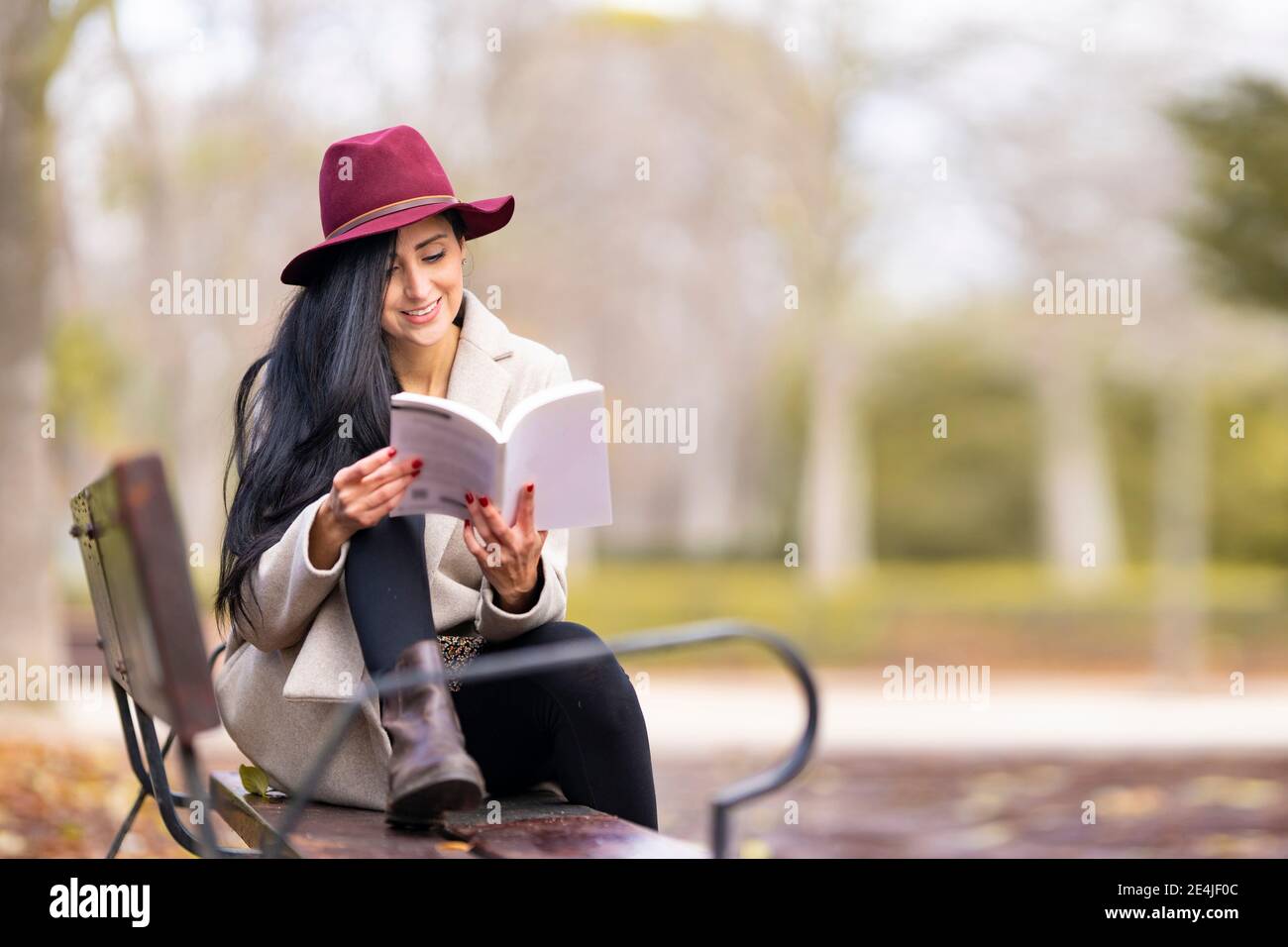 Belle femme avec un livre de lecture de cheveux longs tout en étant assis sur banc dans le parc Banque D'Images