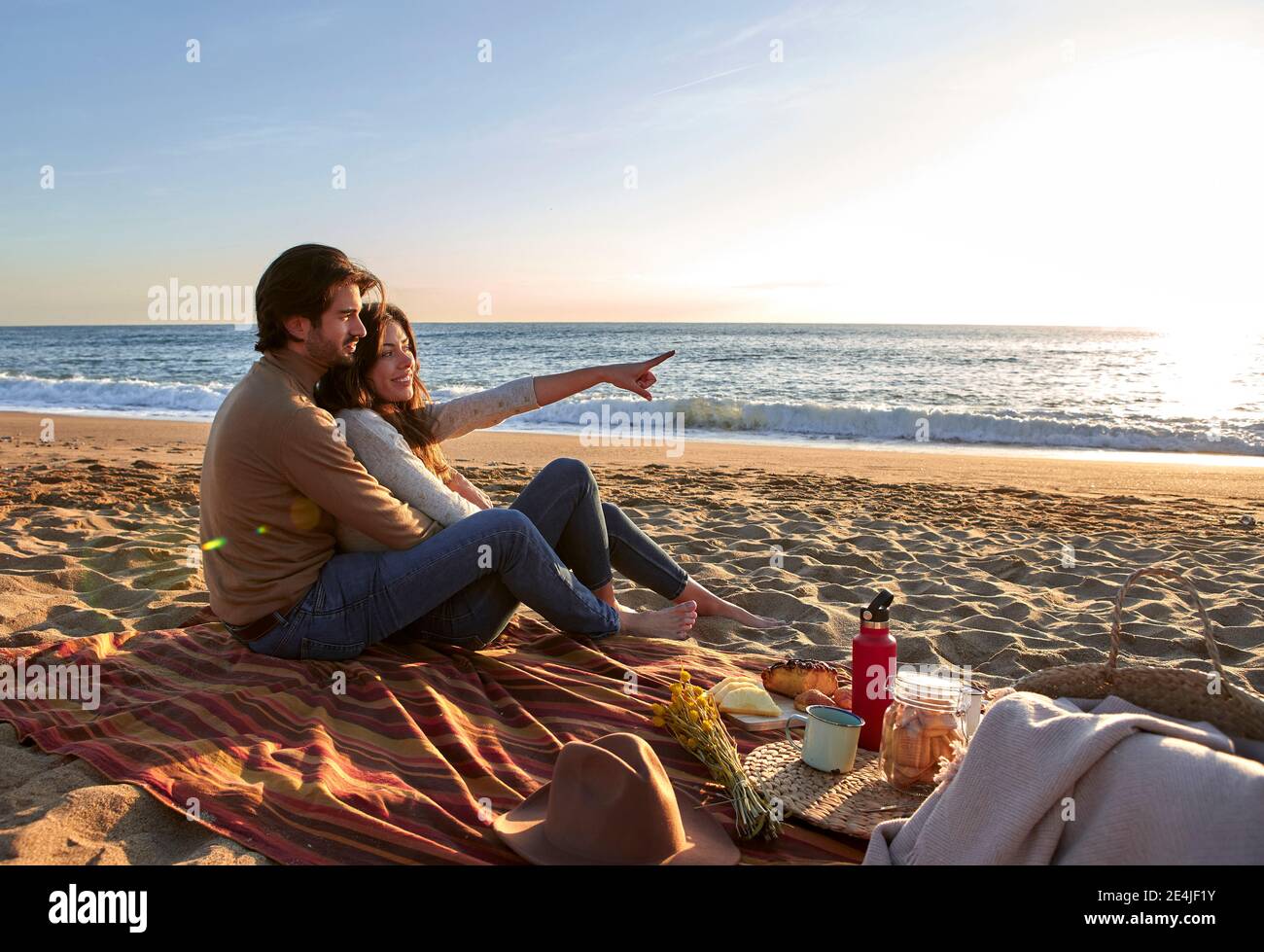 Femme souriante pointant le doigt vers la mer tout en étant assise avec l'homme à plage Banque D'Images