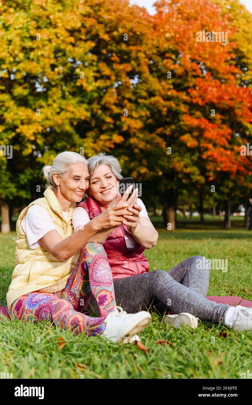 Souriante et mature, des amies vêes de sport prennent le selfie parc d'automne Banque D'Images