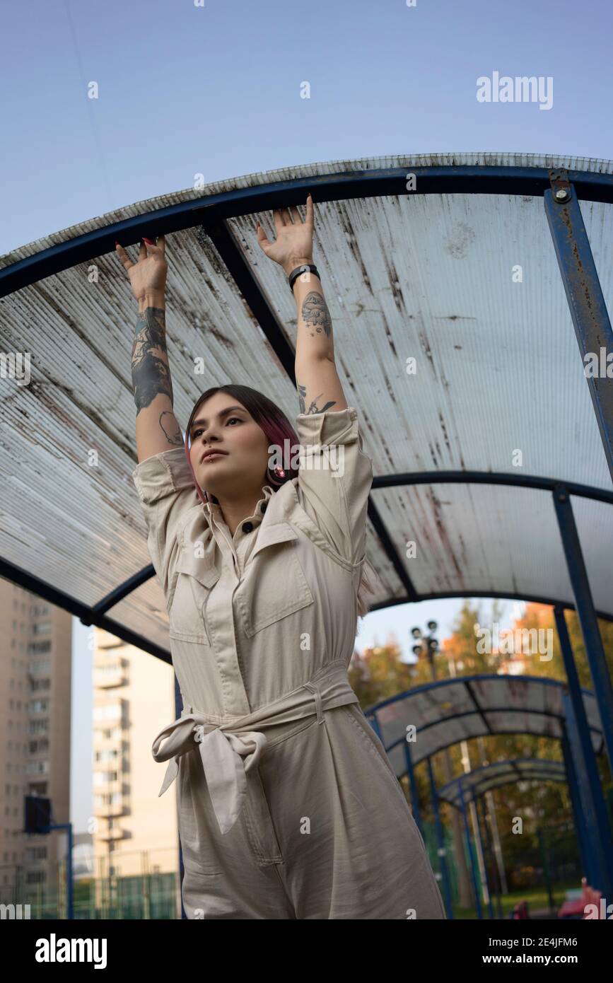 Jeune femme avec tatouage suspendu sur le toit tout en regardant loin sur un terrain de sport Banque D'Images