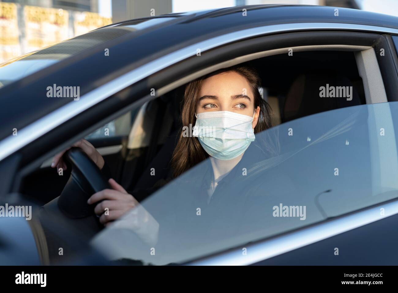 Femme d'affaires portant un masque de protection qui regarde loin en conduisant Pendant COVID-19 Banque D'Images