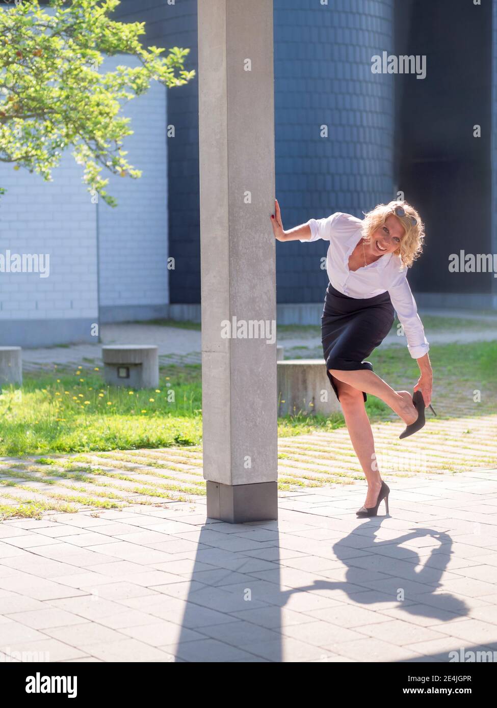 Femme d'affaires souriante portant des talons aiguilles debout près d'une colonne Banque D'Images