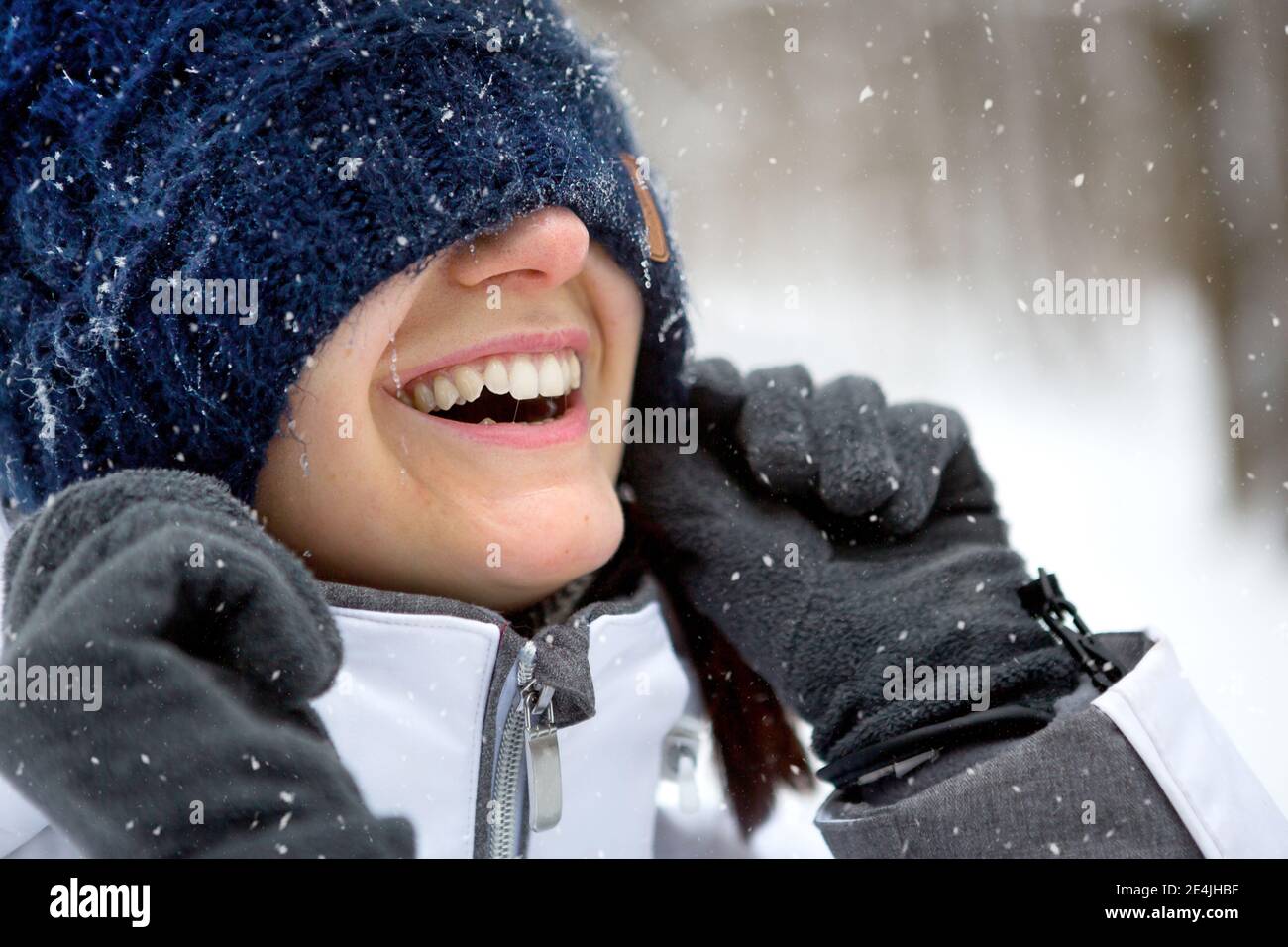 Une femme avec un chapeau tricoté chaud tiré au-dessus de ses yeux sourit et apprécie la neige, le soleil de printemps. Activités de plein air, saisonnalité, hiver, neige fondue. Banque D'Images