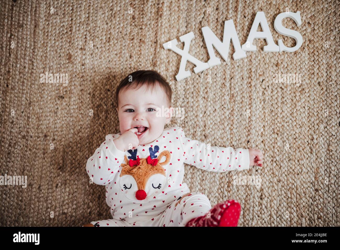 Bébé fille avec le doigt dans la bouche couché sur le sol par Noël texte à la maison Banque D'Images