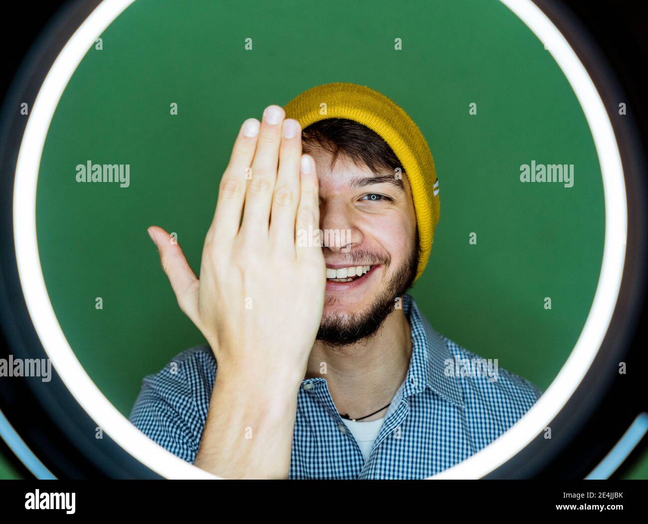 Homme heureux avec flash circulaire cachant visage avec main tout en restant debout sur fond vert Banque D'Images