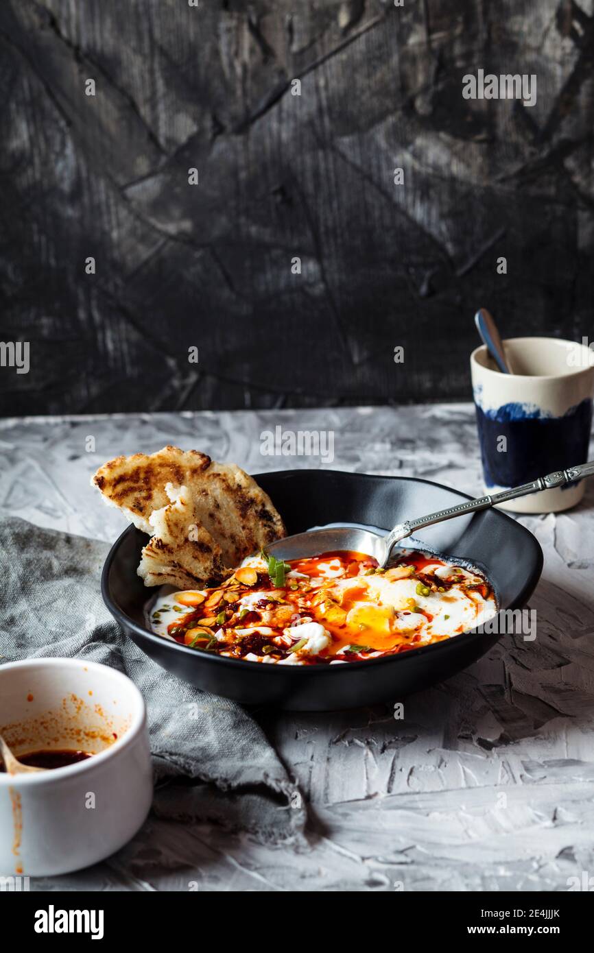 Petit-déjeuner de yaourt et de beurre de paprika épicé sur des œufs pochés dans un bol par une tasse de café sur la table Banque D'Images