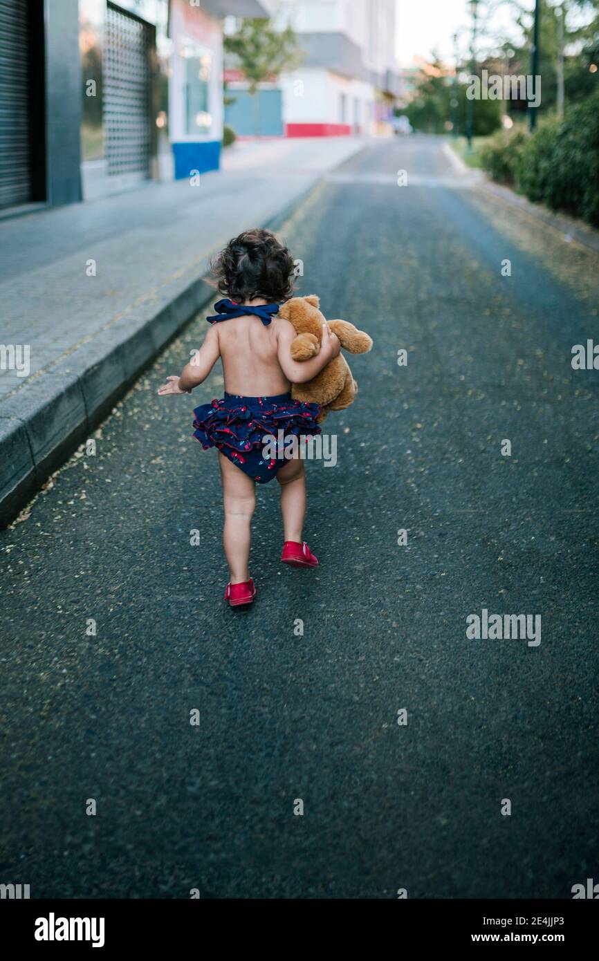 Bébé fille joueur avec ours en peluche qui court sur la route Banque D'Images