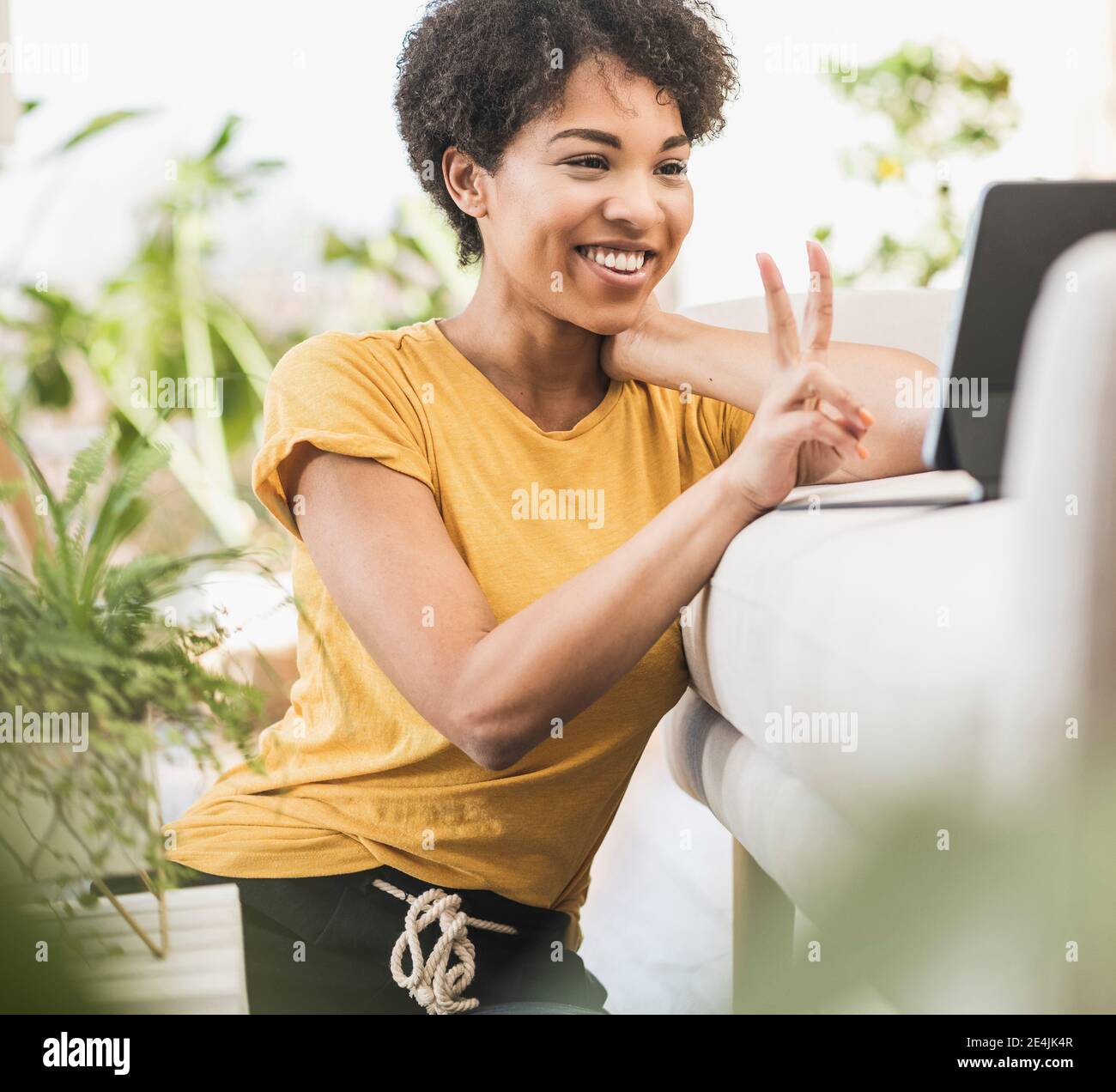 Femme souriante montrant un geste de paix lors d'un appel vidéo via le numérique une tablette à la maison Banque D'Images