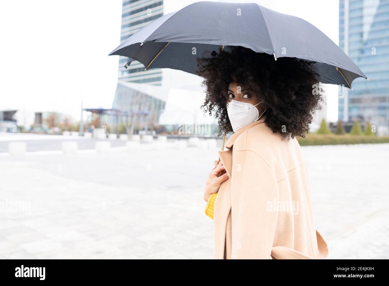 Jeune femme portant un masque de protection tenant un parapluie debout à l'extérieur Banque D'Images