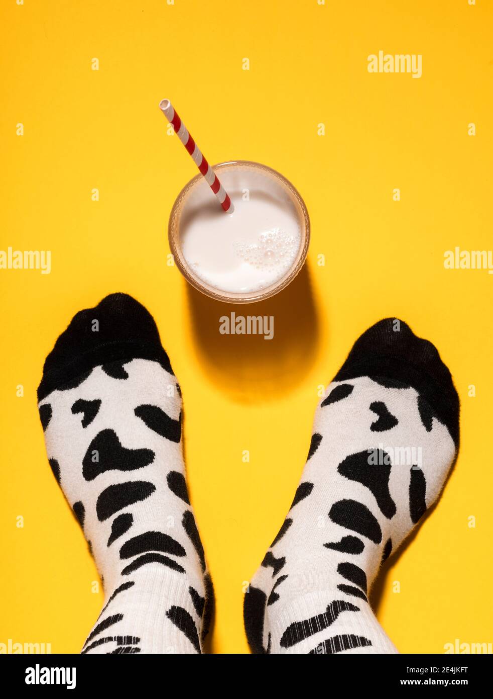 Pied d'homme avec chaussettes à imprimé vache et verre de lait sur fond jaune Banque D'Images