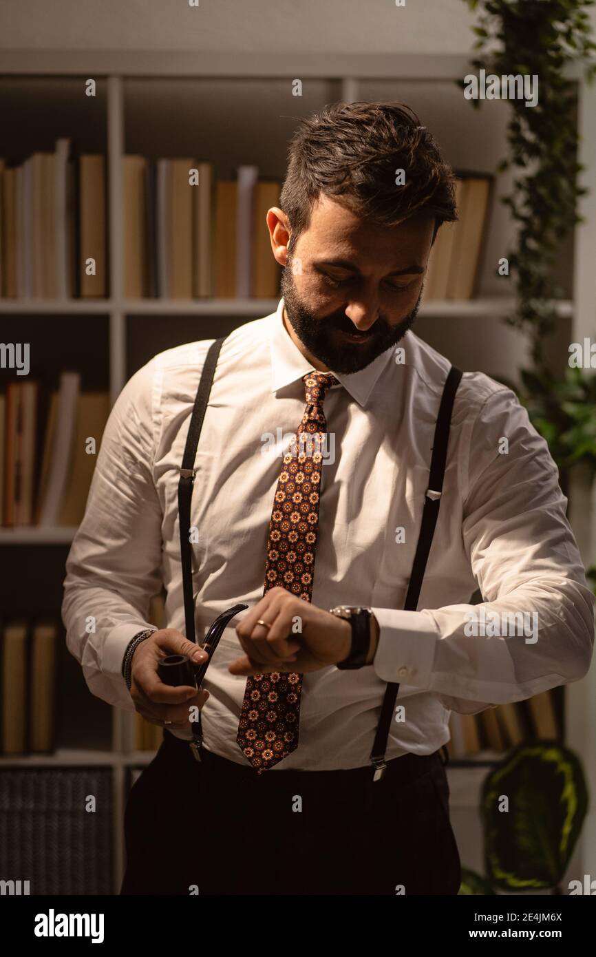Portrait de l'homme barbu qui vérifie le temps avec le tuyau de fumée main Banque D'Images