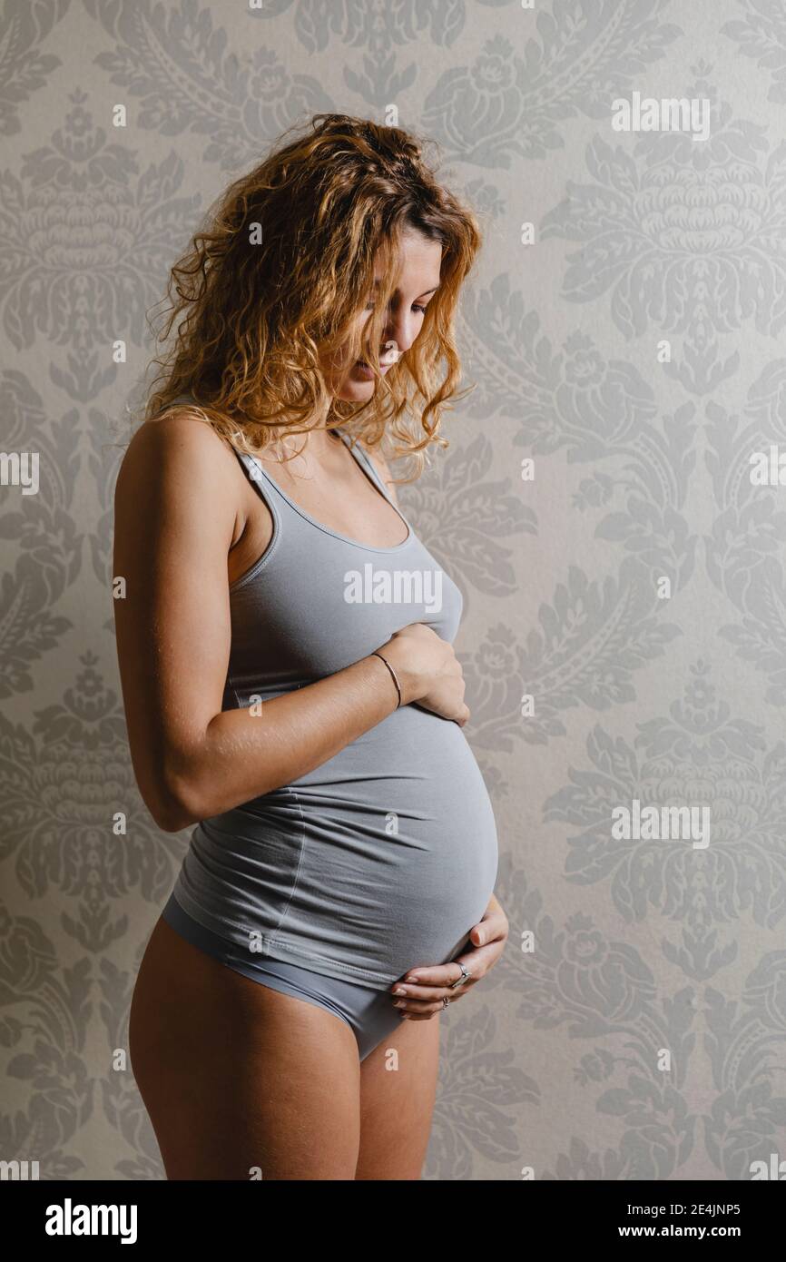 Jeune enceinte touchant l'abdomen contre le mur à la maison Banque D'Images