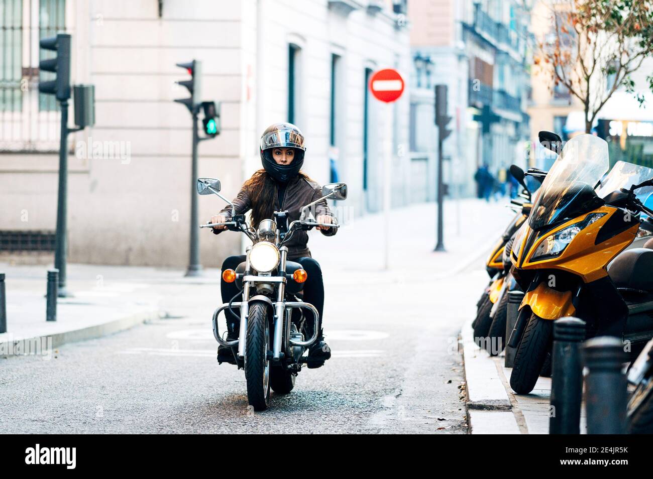 Femme de motard dans un casque portant une veste en cuir tout en regardant loin en ville Banque D'Images