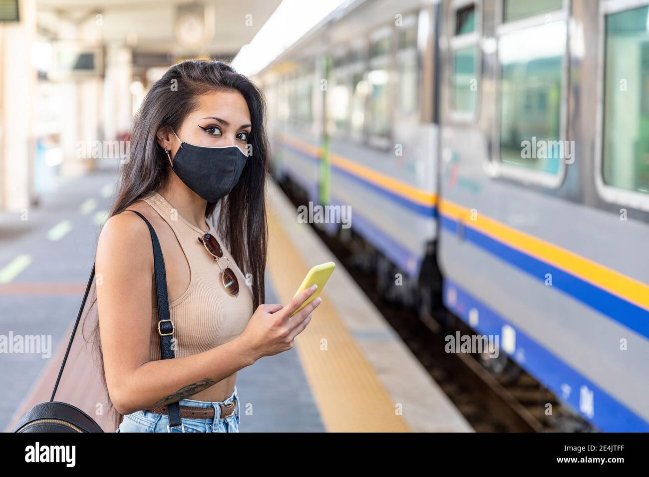 Jeune femme portant un masque facial avec un téléphone portable debout sur la plate-forme Banque D'Images