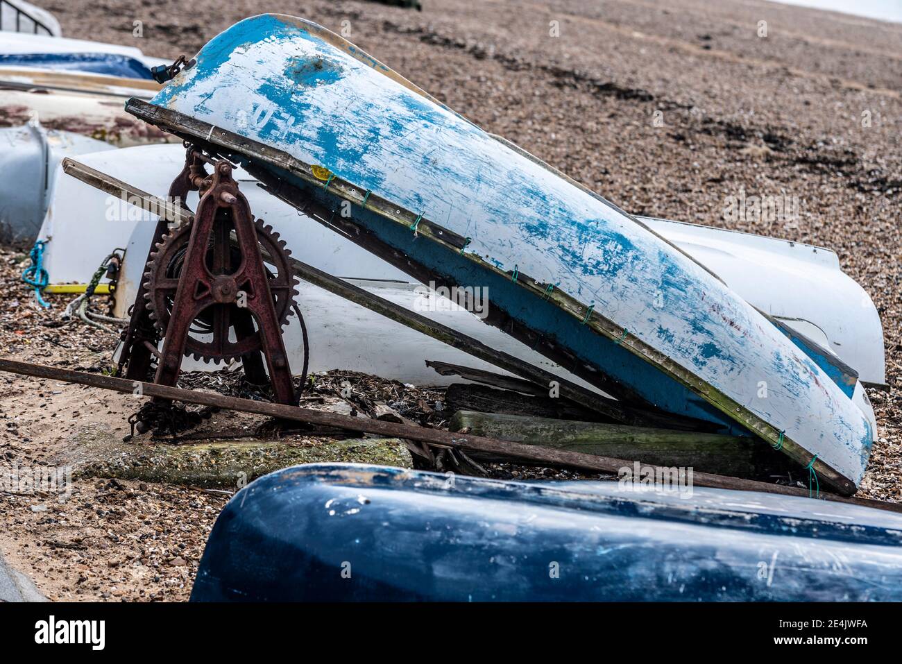 Vieux bateau à ramer, canot, retourné, soutenu contre le cadre de manivelle rouillé pour créer un abri. Mécanisme d'enroulement corrodé. Treuil Banque D'Images