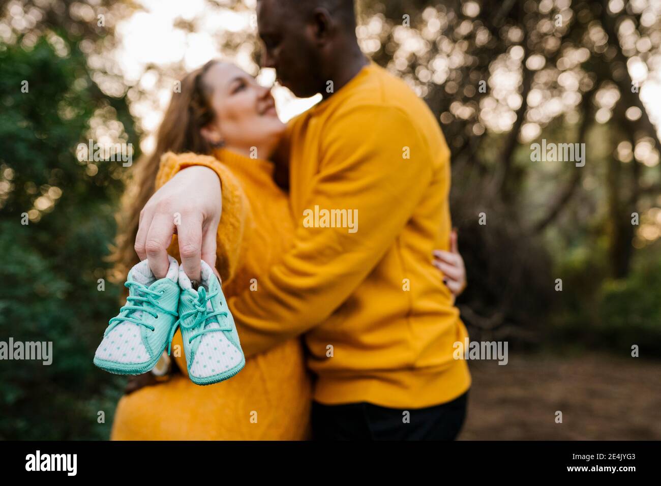 Femme enceinte tenant la chaussure de bébé tout en embrassant l'homme debout à forêt Banque D'Images