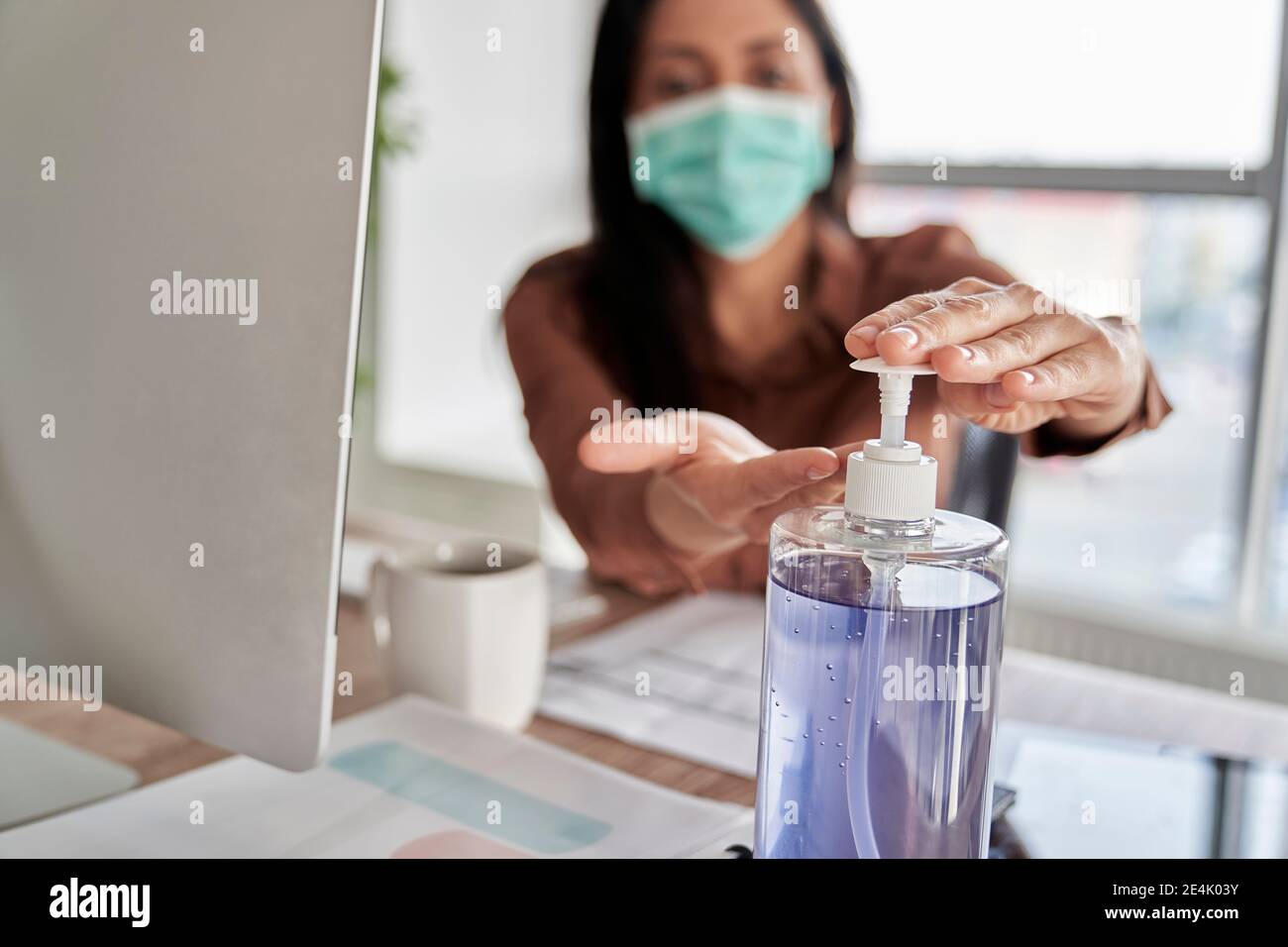 Femme d'affaires se nettoyant les mains avec un assainisseur au bureau Banque D'Images