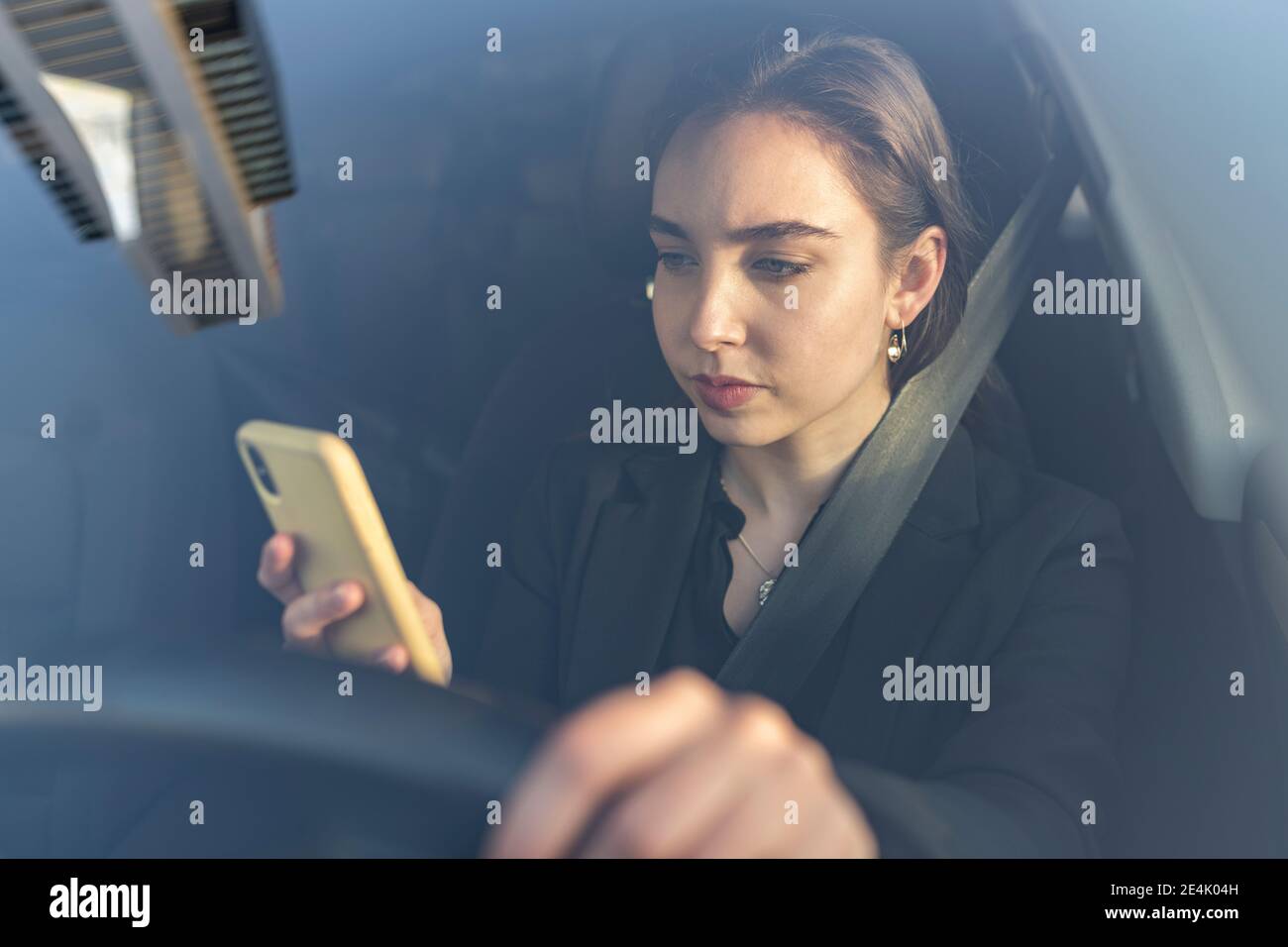 Jeune femme d'affaires utilisant un téléphone mobile en étant assise dans la voiture Banque D'Images