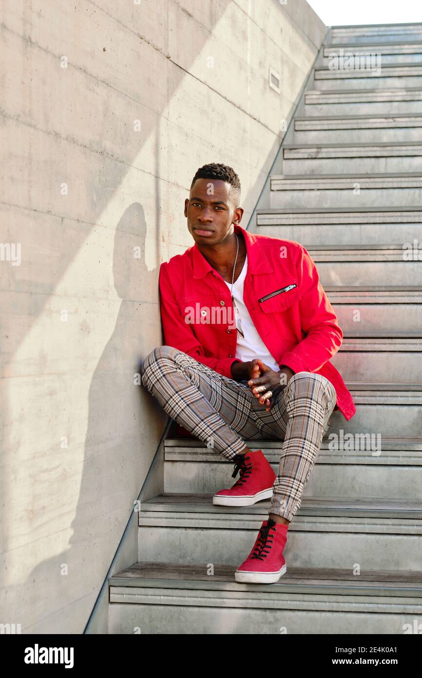 Portrait d'un jeune homme en veste rouge et pantalon à carreaux assis sur  des marches à l'extérieur Photo Stock - Alamy