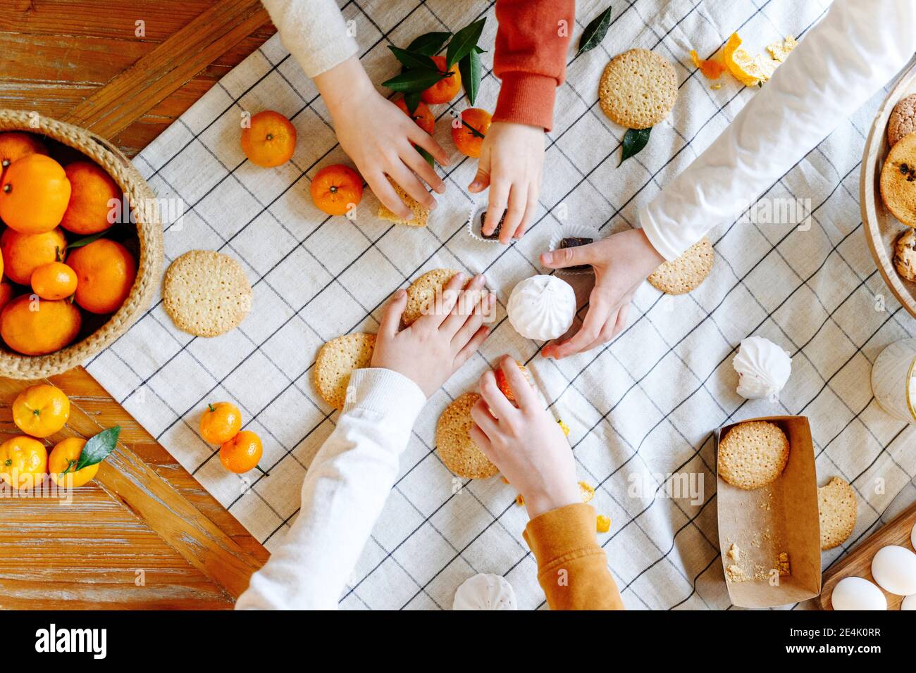 Mains de frères et sœurs prenant des biscuits et des mandarines sur la table à accueil Banque D'Images