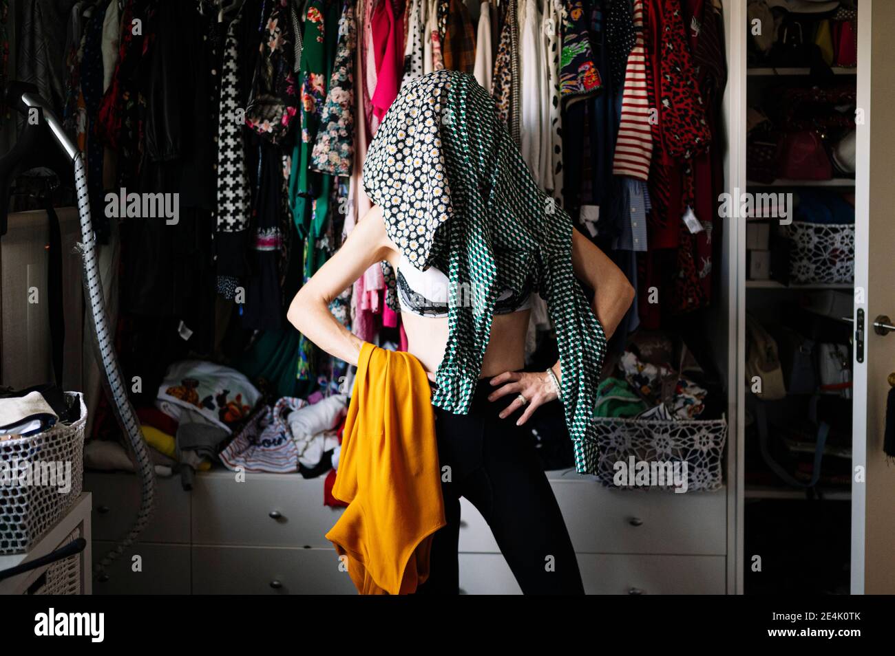 Femme en robe verte à pois portant des chaussures blanches contre des vêtements suspendus dans un rack à l'appartement Banque D'Images