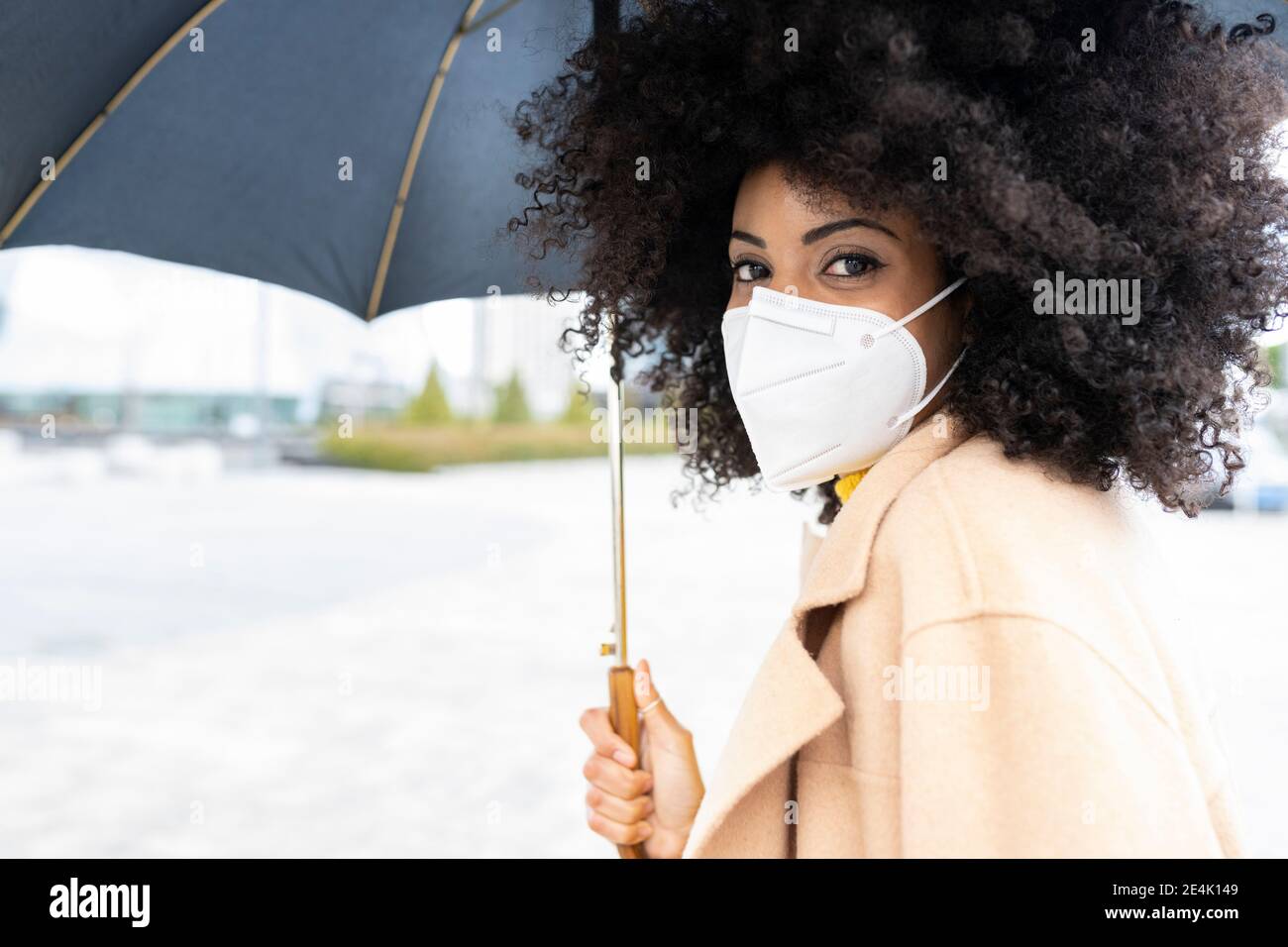 Femme avec masque de visage tenant un parapluie en se tenant debout à l'extérieur Banque D'Images