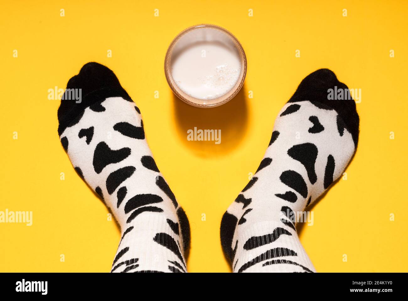 Pied d'homme avec chaussettes à imprimé vache et verre de lait sur fond jaune en studio Banque D'Images