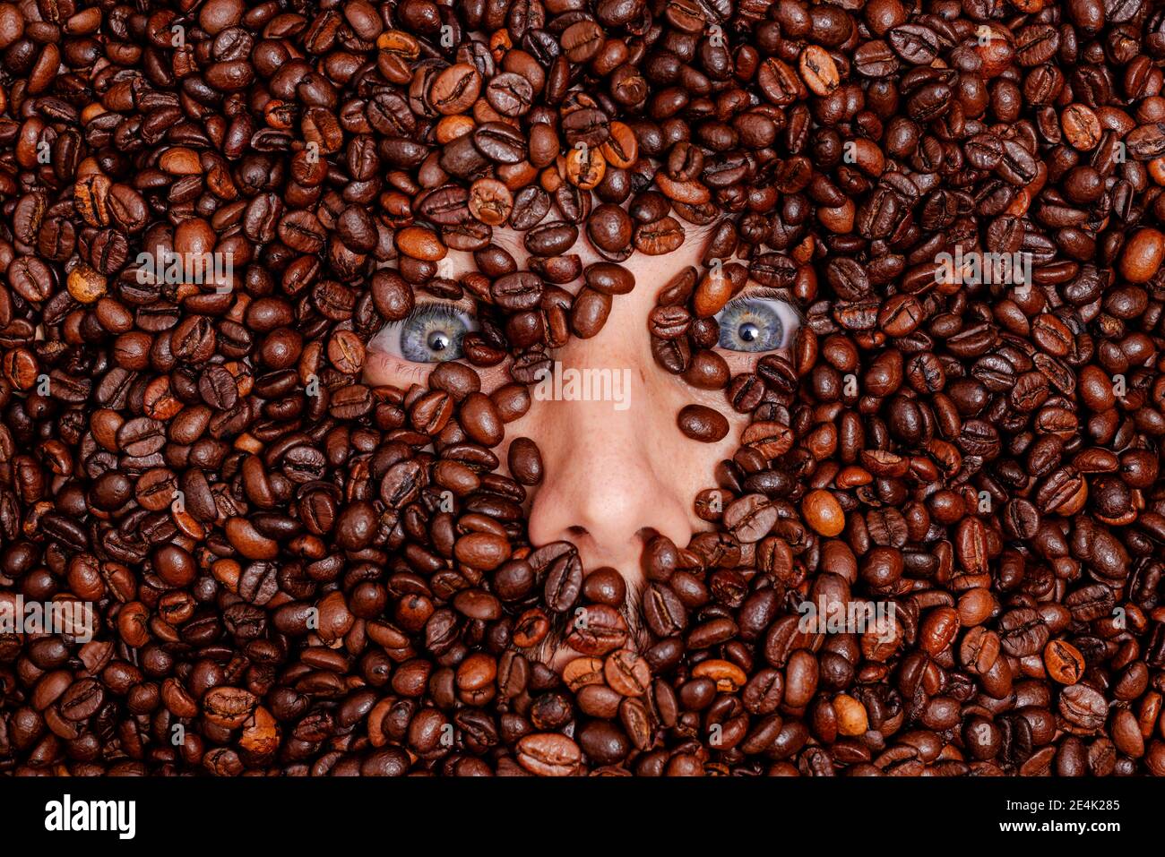 Visage humain enterré dans des grains de café torréfiés Banque D'Images