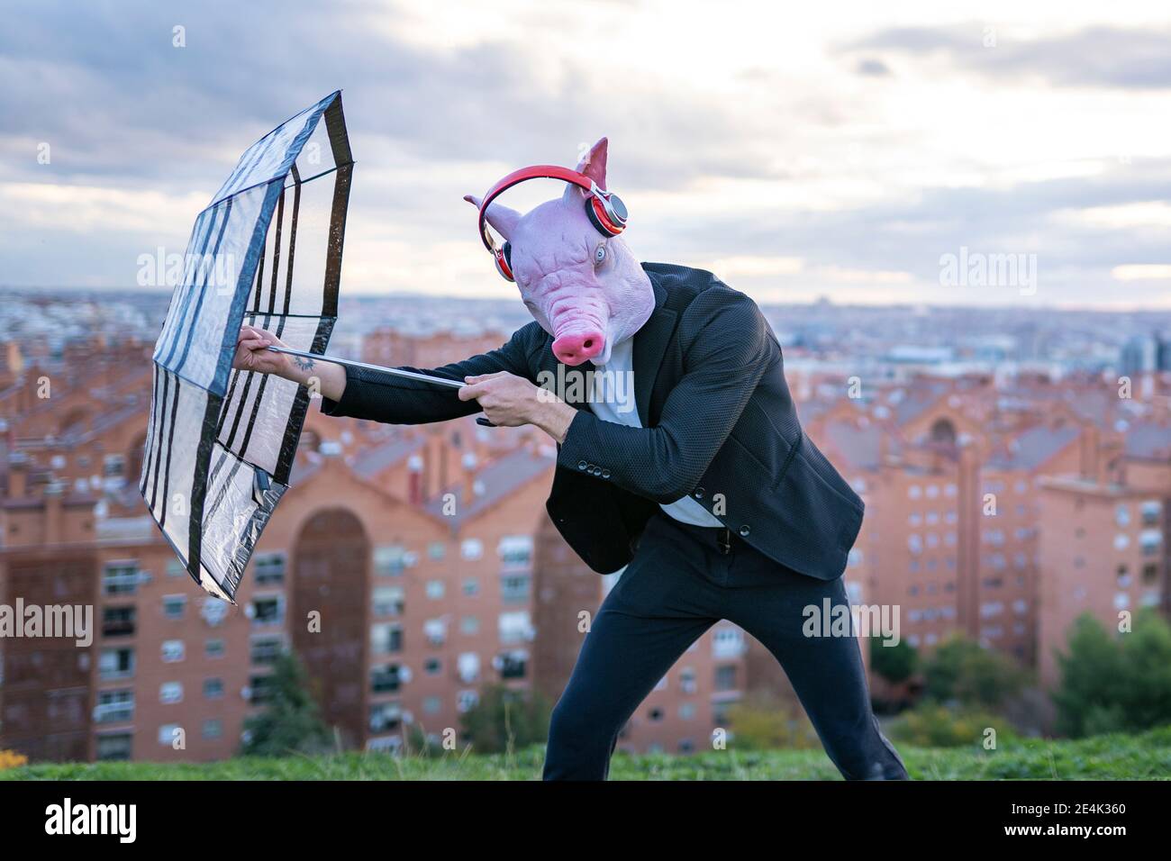 Homme entrepreneur portant un masque de porc et un casque sans fil aux prises parapluie contre le ciel Banque D'Images