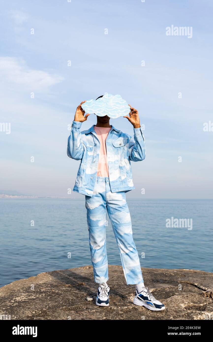 Un jeune homme se cachant face avec un nuage coupé en se tenant debout contre la mer Banque D'Images