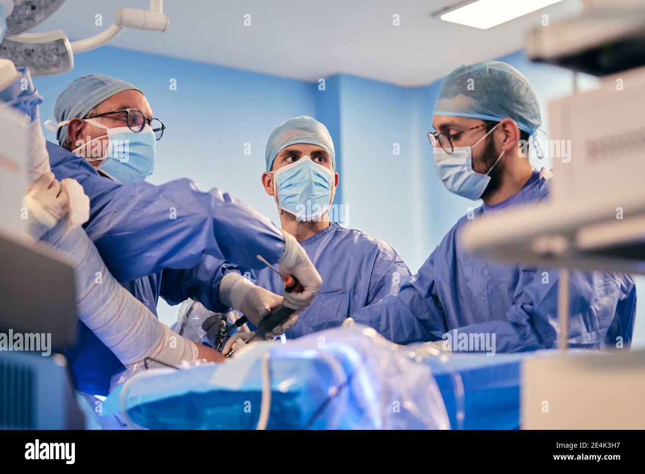 Les médecins de sexe masculin qui opèrent une chirurgie avec un équipement chirurgical tout en étant debout Salle d'opération pendant COVID-19 Banque D'Images