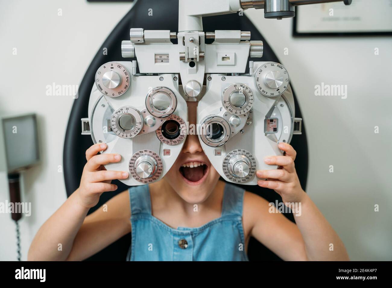 Fille gaie avec la bouche ouverte tenant l'équipement de test d'oeil dedans clinique Banque D'Images